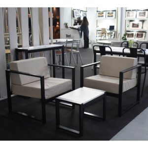 Dos sillones modelo Lena con estructura de caño negro y cojines beige, junto a una mesa ratona a juego en una exhibición.