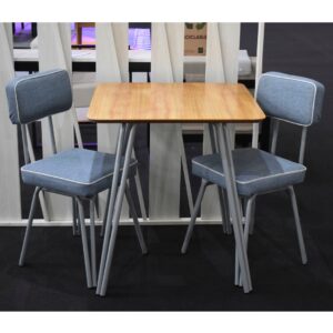 Mesa cuadrada de madera con dos sillas de caño tapizadas en azul, estilo vintage, sobre una alfombra oscura.