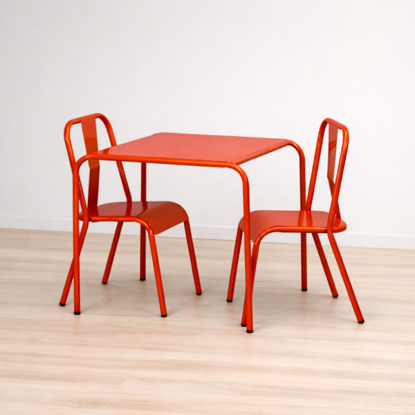 Mesa cuadrada y dos sillas metálicas rojas sobre suelo de madera clara, con pared blanca de fondo.
