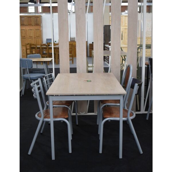 Juego de comedor con mesa cuadrada de madera clara y cuatro sillas de caño gris con asientos marrones en una exposición.