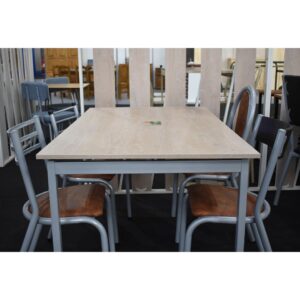 Mesa de comedor Dora con tapa de madera clara y cuatro sillas de caño gris con asientos tapizados en marrón.